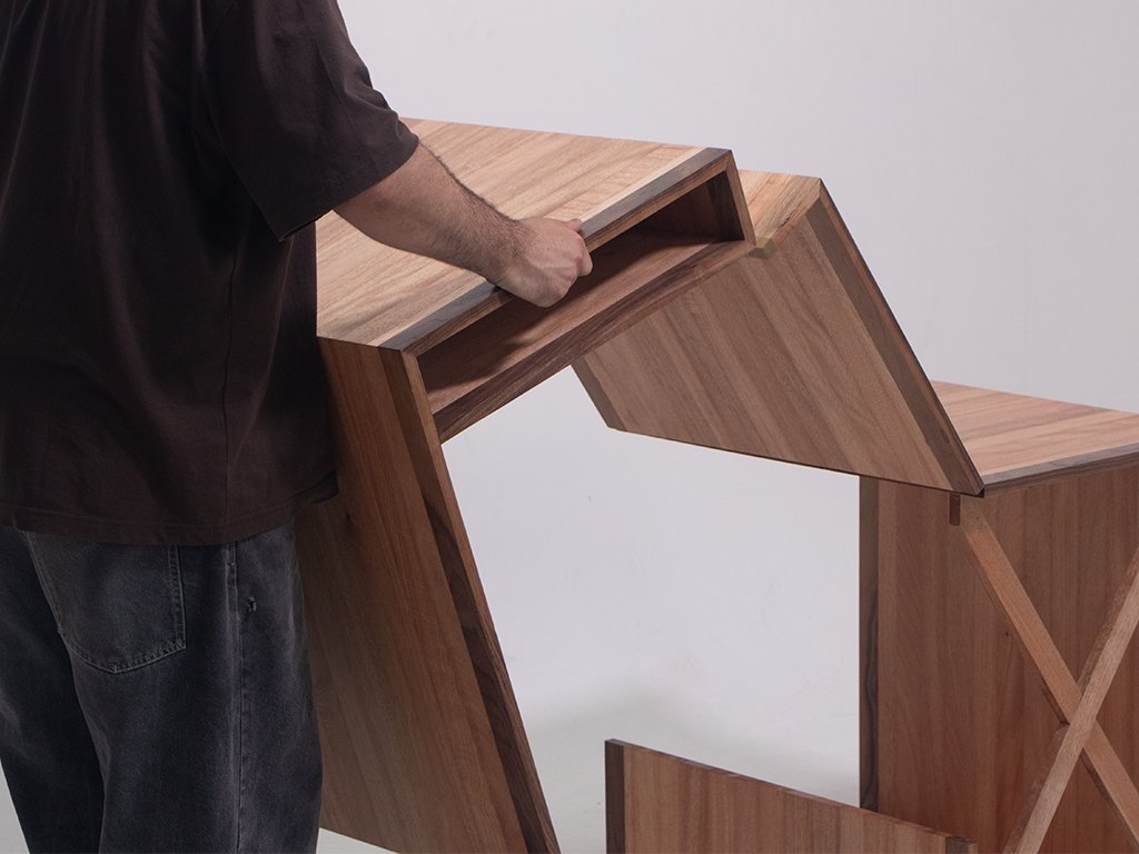 A view of STRIATO in use. The table is divided into three sections, with the third on one side remaining stationary as the user folds the other end to create a more compact form. The choice of Okoumé and edgebanded Walnut makes the table lightweight and easy to move making it suitable for smaller spaces.